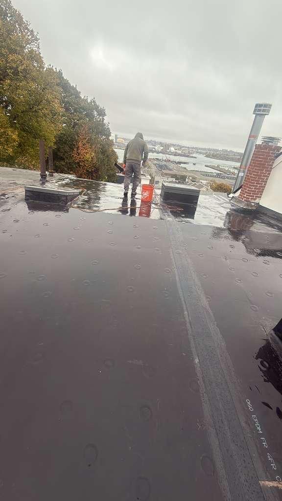 Person standing on a wet, flat roof with a cityscape in the background; overcast sky.