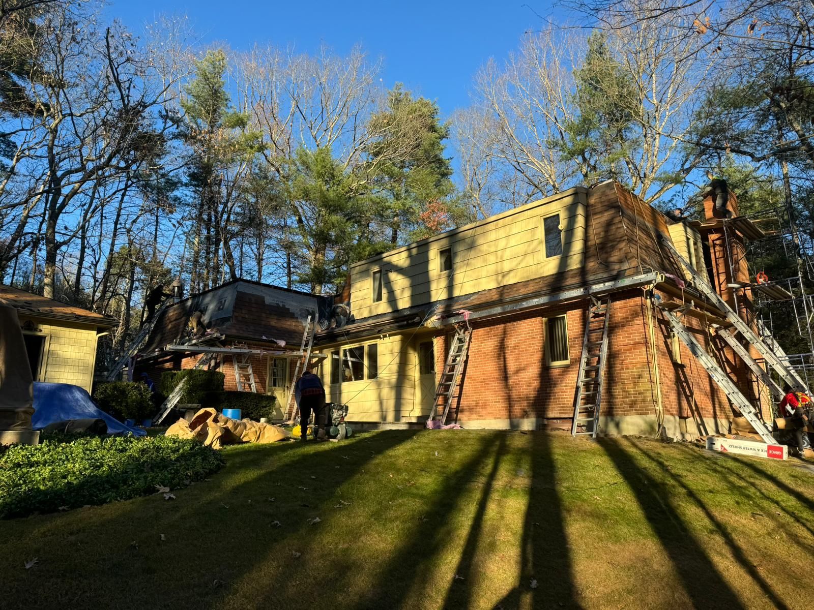 House under construction, ladders, exposed wood, brick, trees, sunny day.