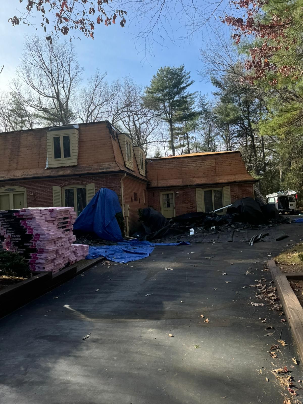 Roofing materials and debris on a driveway in front of a house. The roof is partially torn off.