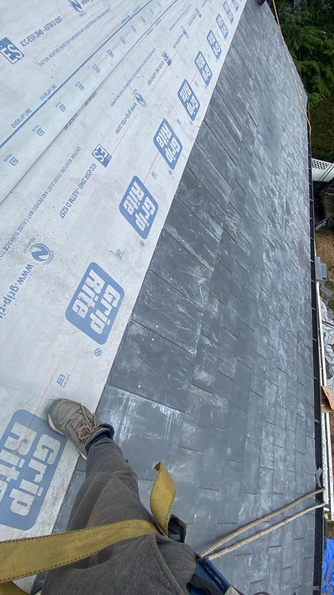 Person on roof wearing harness, installing underlayment. Grip Rite brand visible.