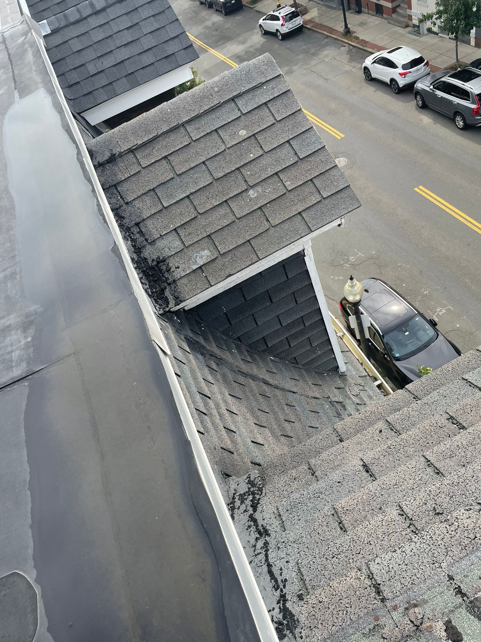 View from a rooftop, showing weathered rooftops, a street with cars, and wet surfaces.