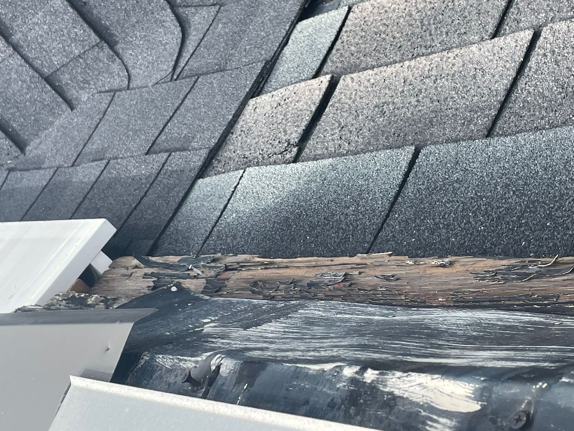 Close-up of a damaged roof edge showing worn shingles, exposed rotting wood, and a gutter.