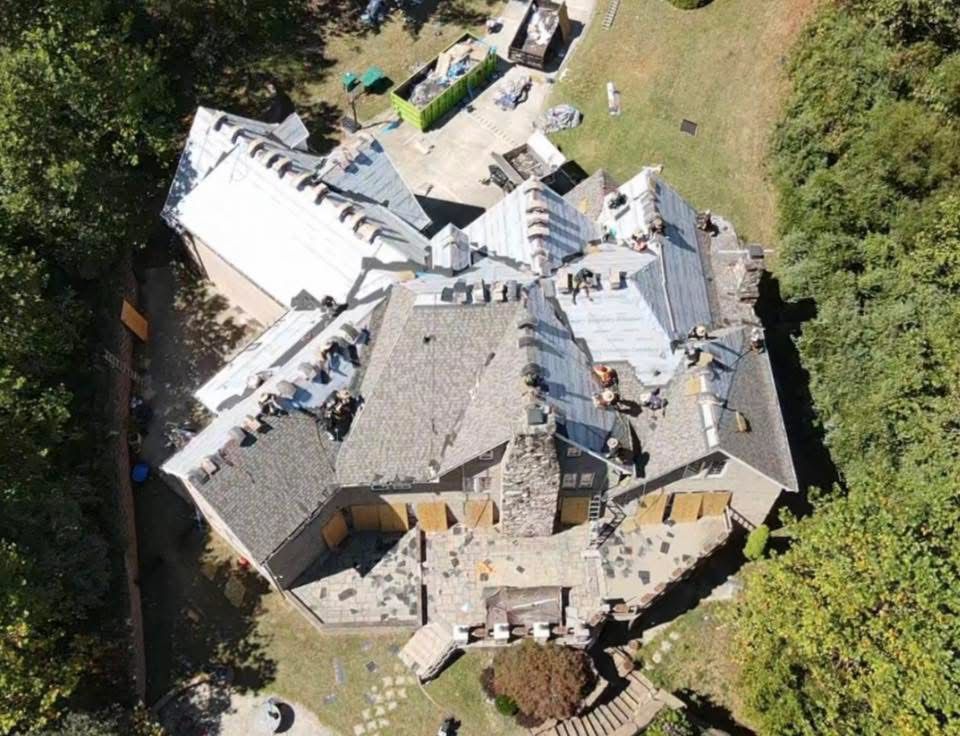 Aerial view of a house undergoing a roof replacement with workers and materials visible.