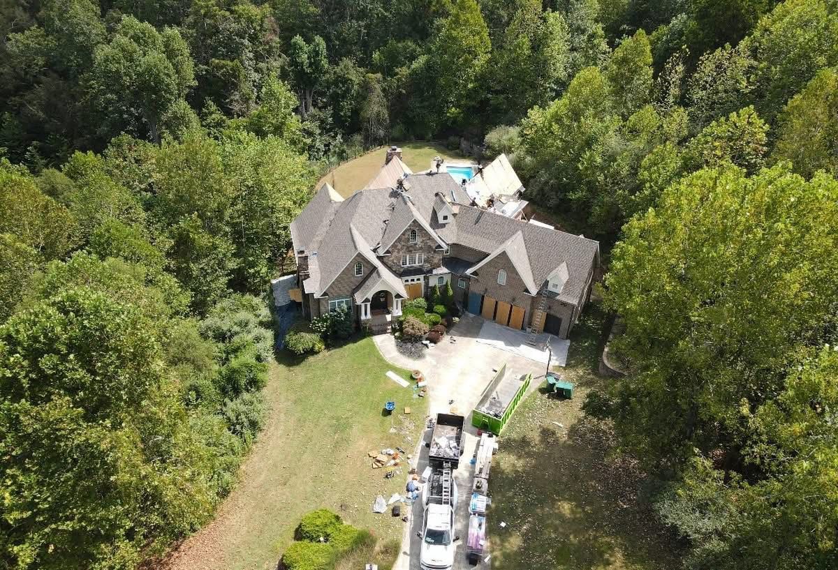 Aerial view of a large house with a stone exterior surrounded by trees and a pool.