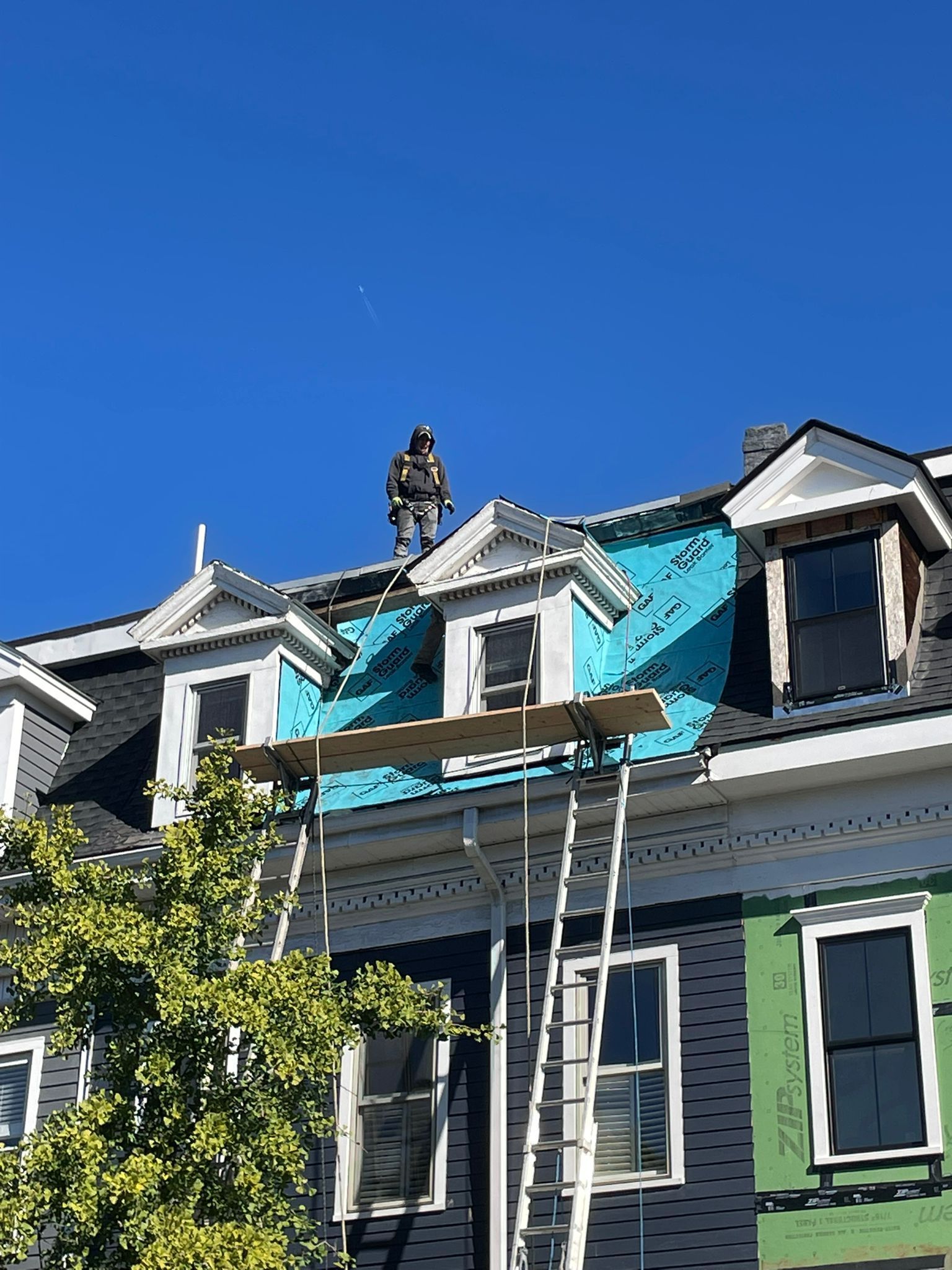 Person on rooftop installing roofing; scaffolding, blue sky.