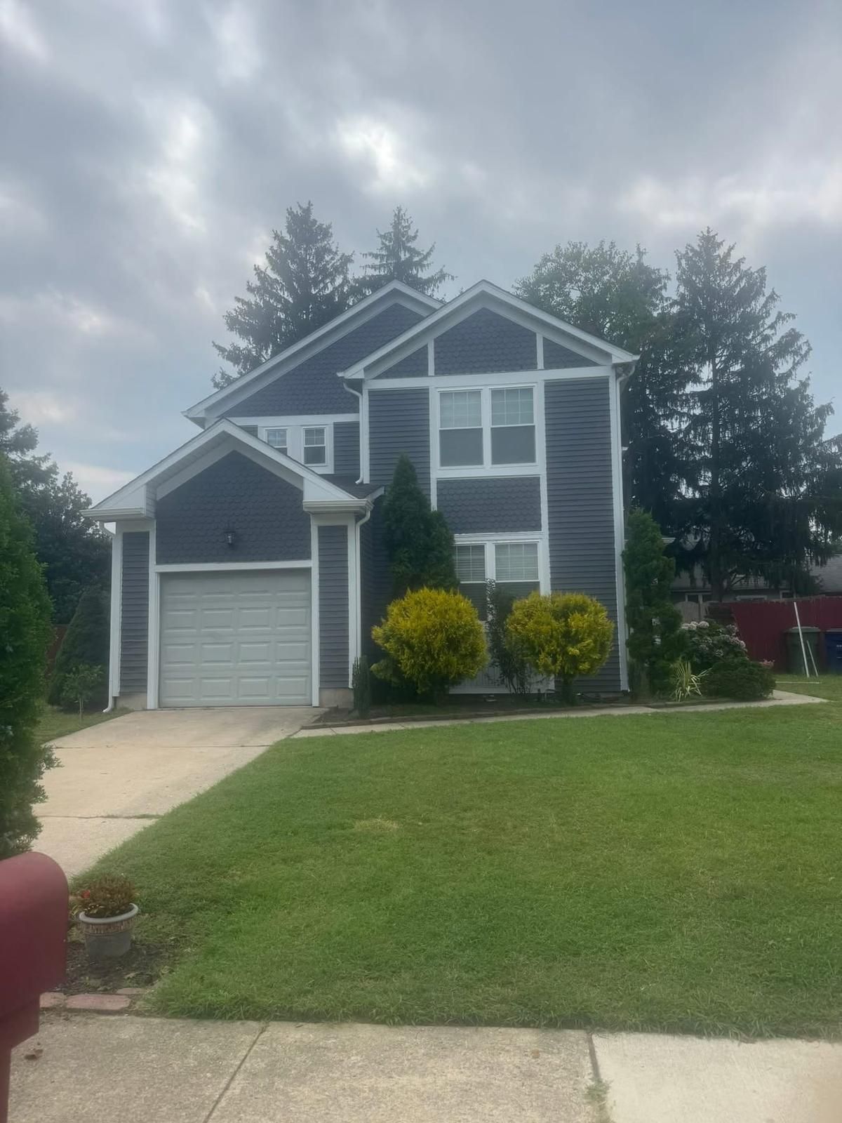 Two-story house with dark gray siding, light gray garage door, and green lawn under cloudy sky.