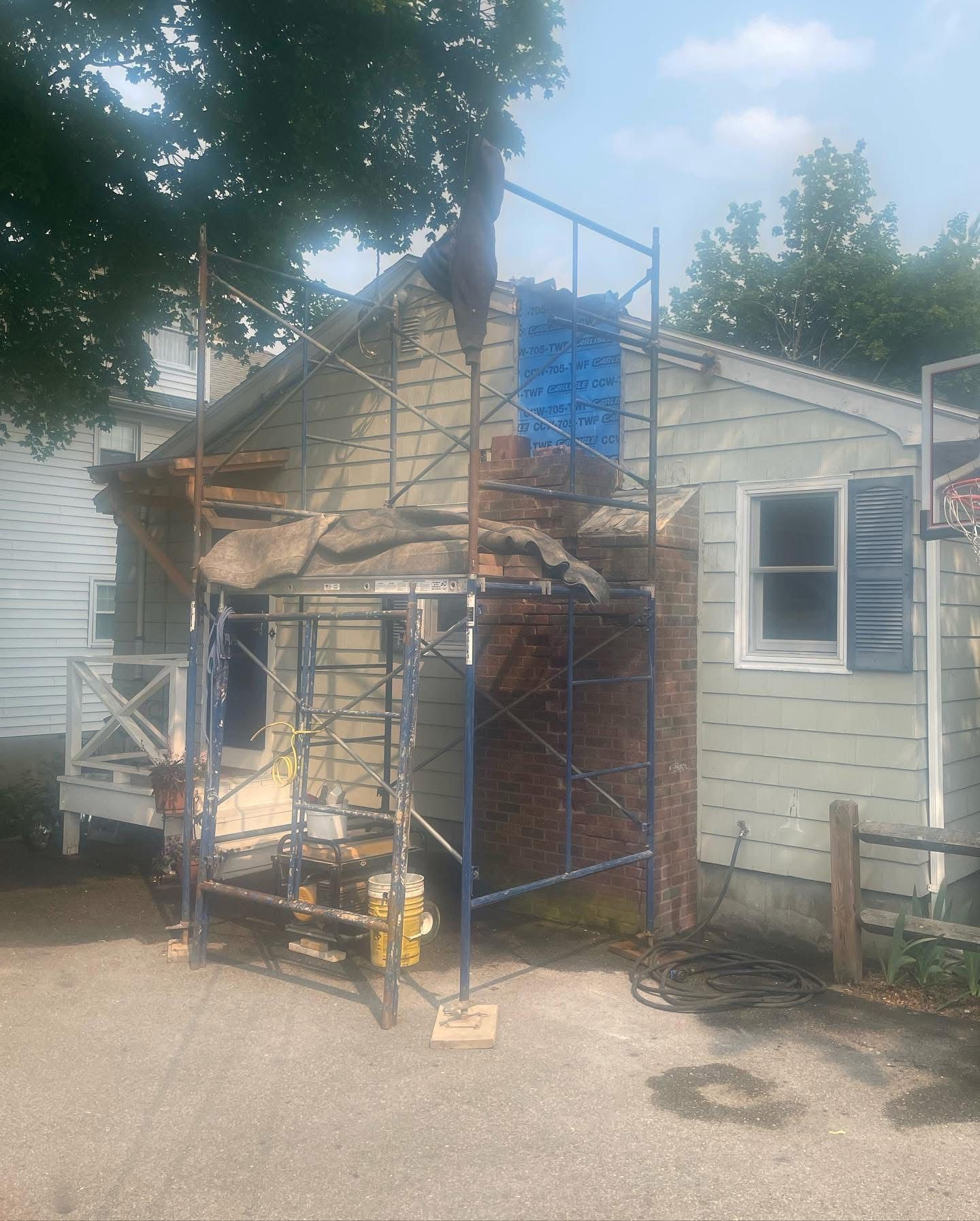 House exterior with scaffolding around brick chimney, undergoing repair.
