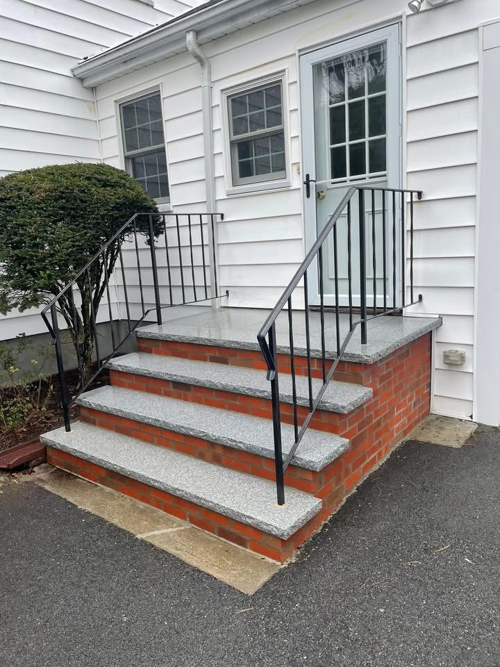 Brick steps with granite treads leading to a white house door, black railing.