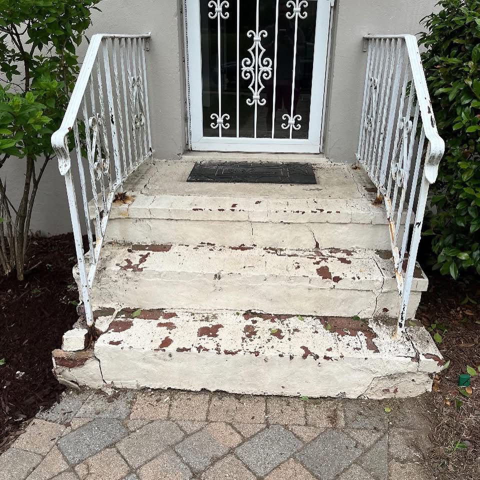 White concrete steps leading to a door with ornate ironwork; white railing.