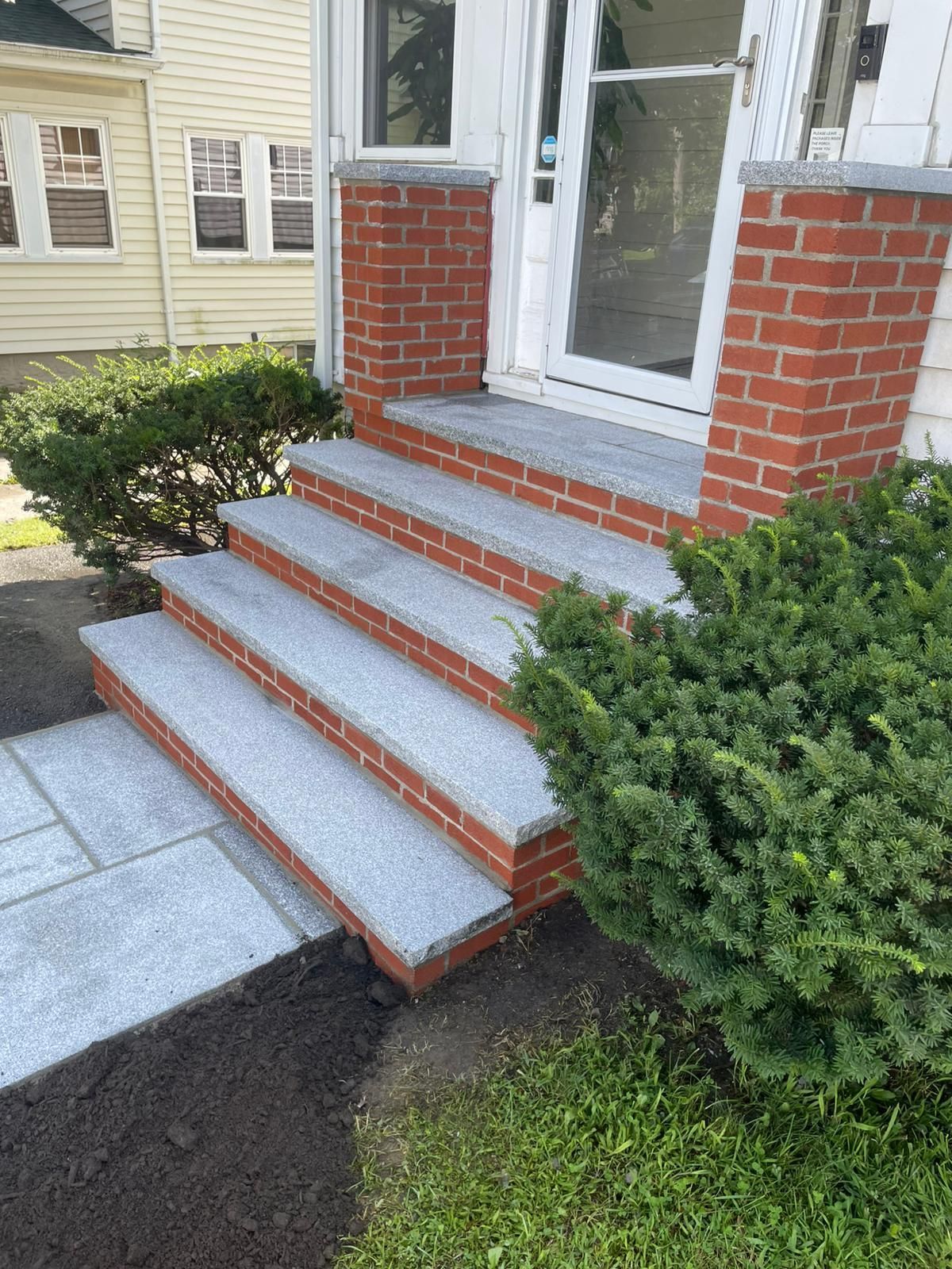 Brick and stone steps leading to a white door, flanked by greenery and red brick columns.
