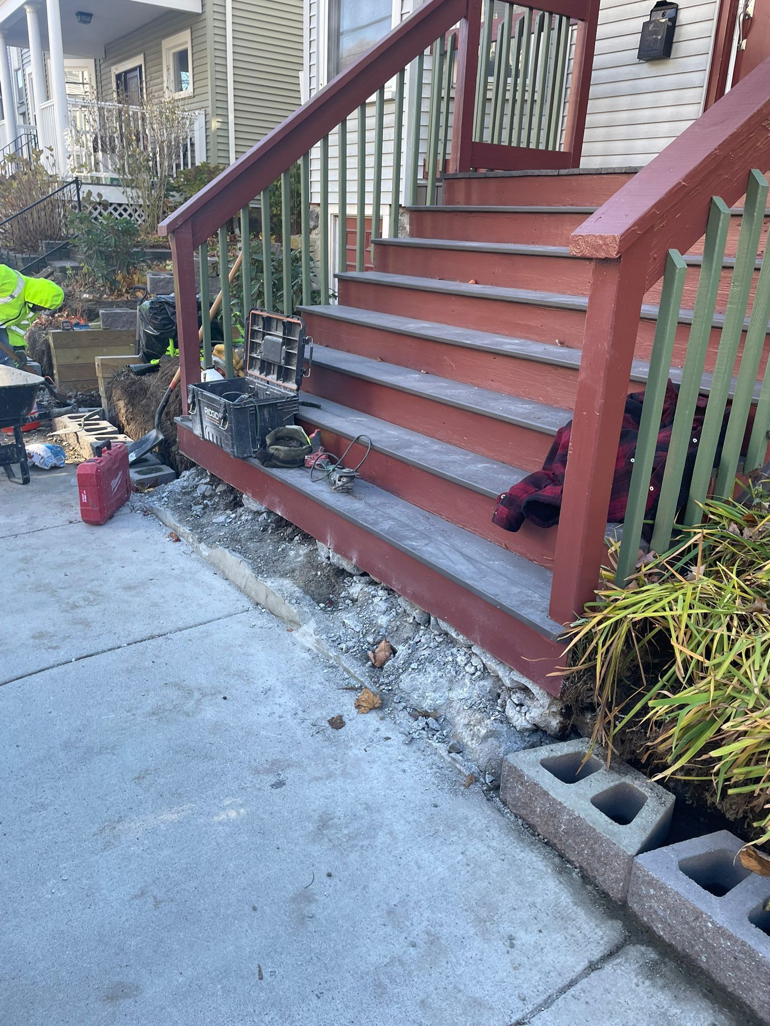 Red wooden stairs leading to a building's entrance, with concrete damage at the base.