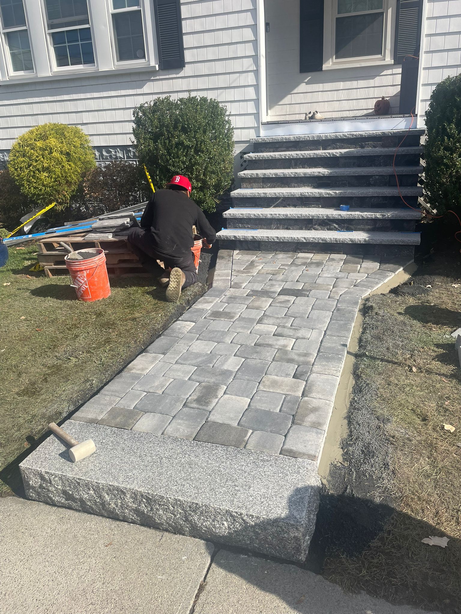 A worker installing a brick walkway and steps leading to a house.