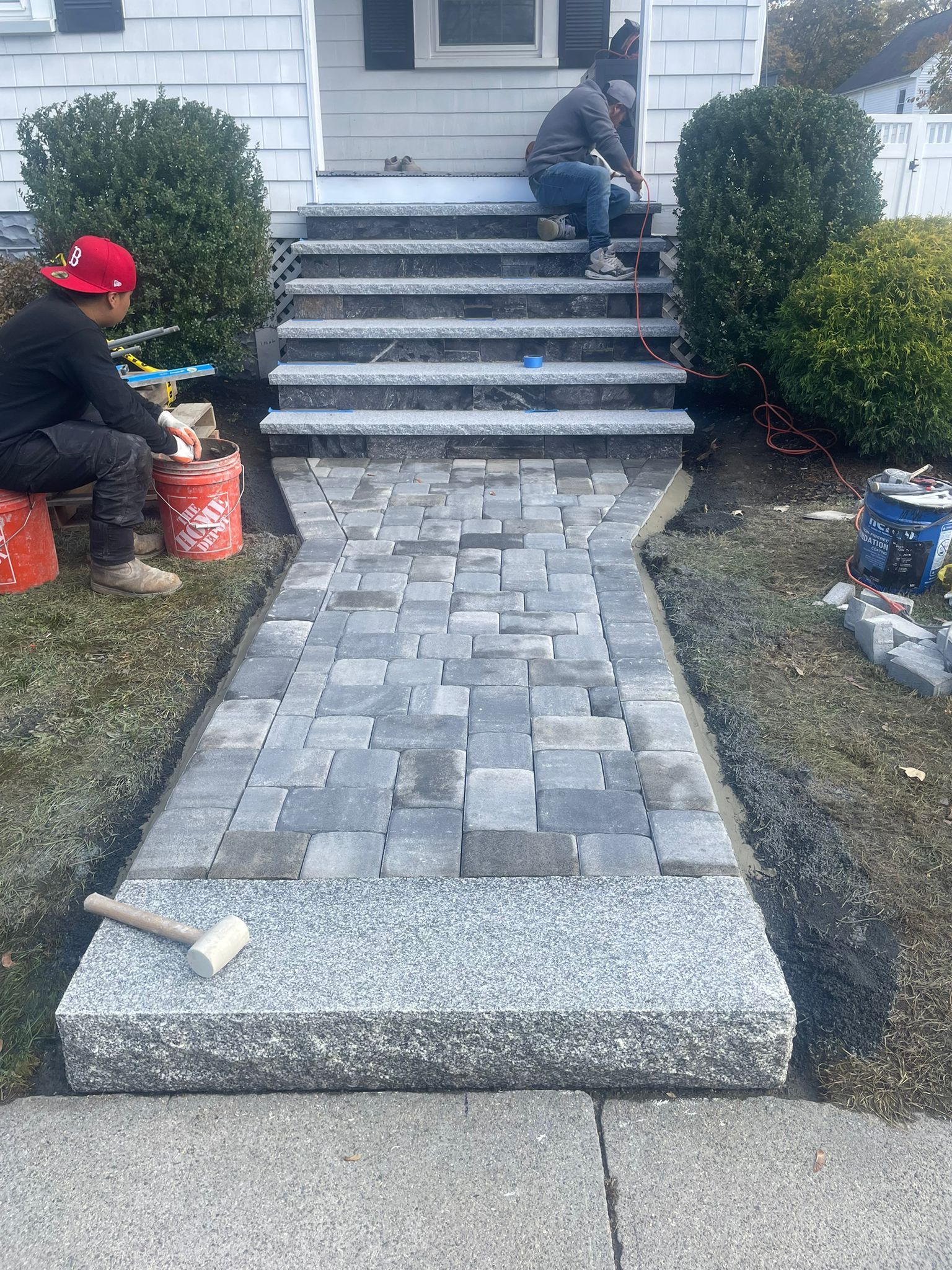 Workers installing a brick pathway and steps leading to a house entrance.