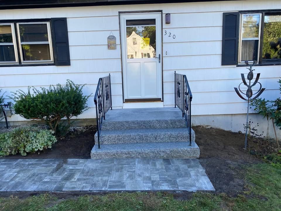 Front entrance with steps and walkway leading to a white door. Black handrails, gray steps, and gray brick walkway.