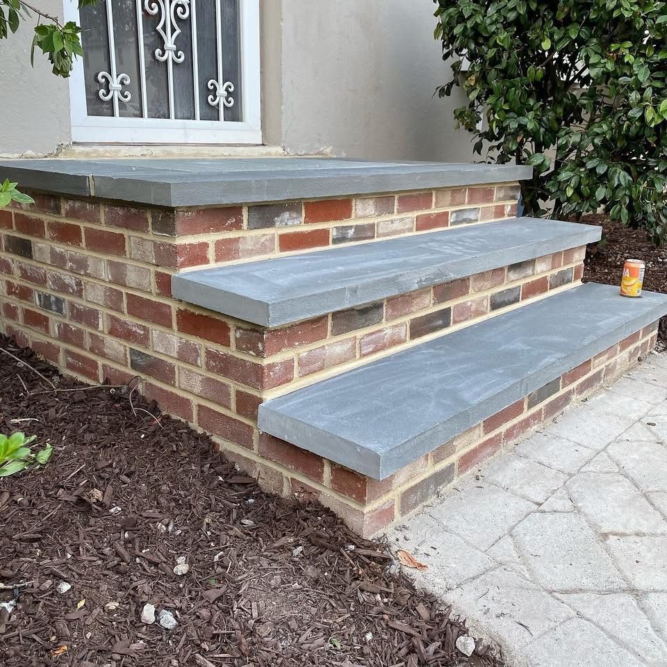 Brick steps with gray stone treads leading to a door with a metal security grill.