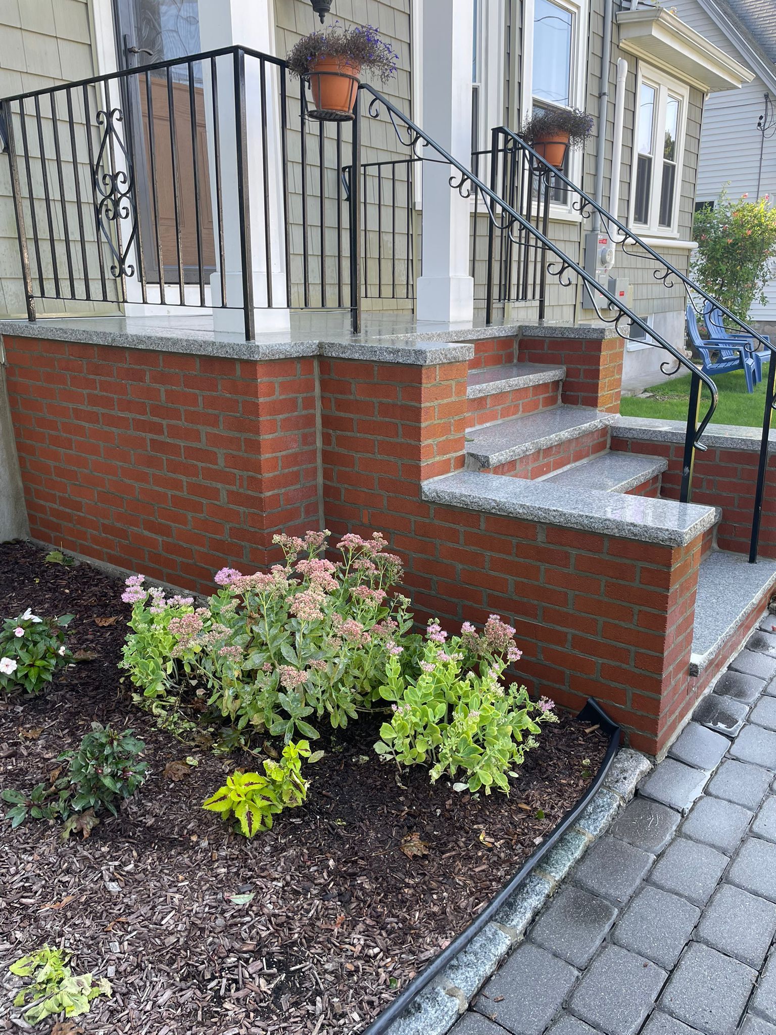 Brick front porch with steps and landscaping; railing, flower pots, and stone trim.