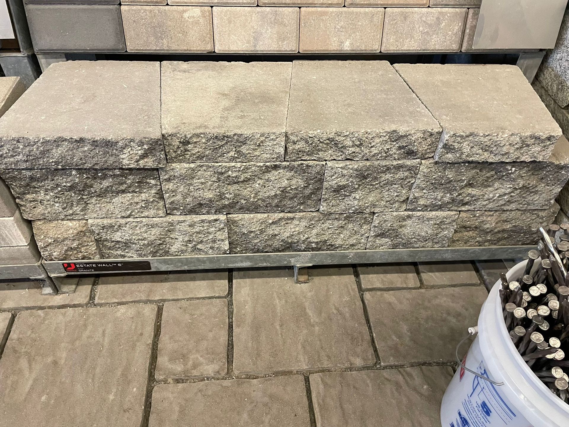 Stacked retaining wall blocks on a metal rack, with a bucket of sticks in the foreground.