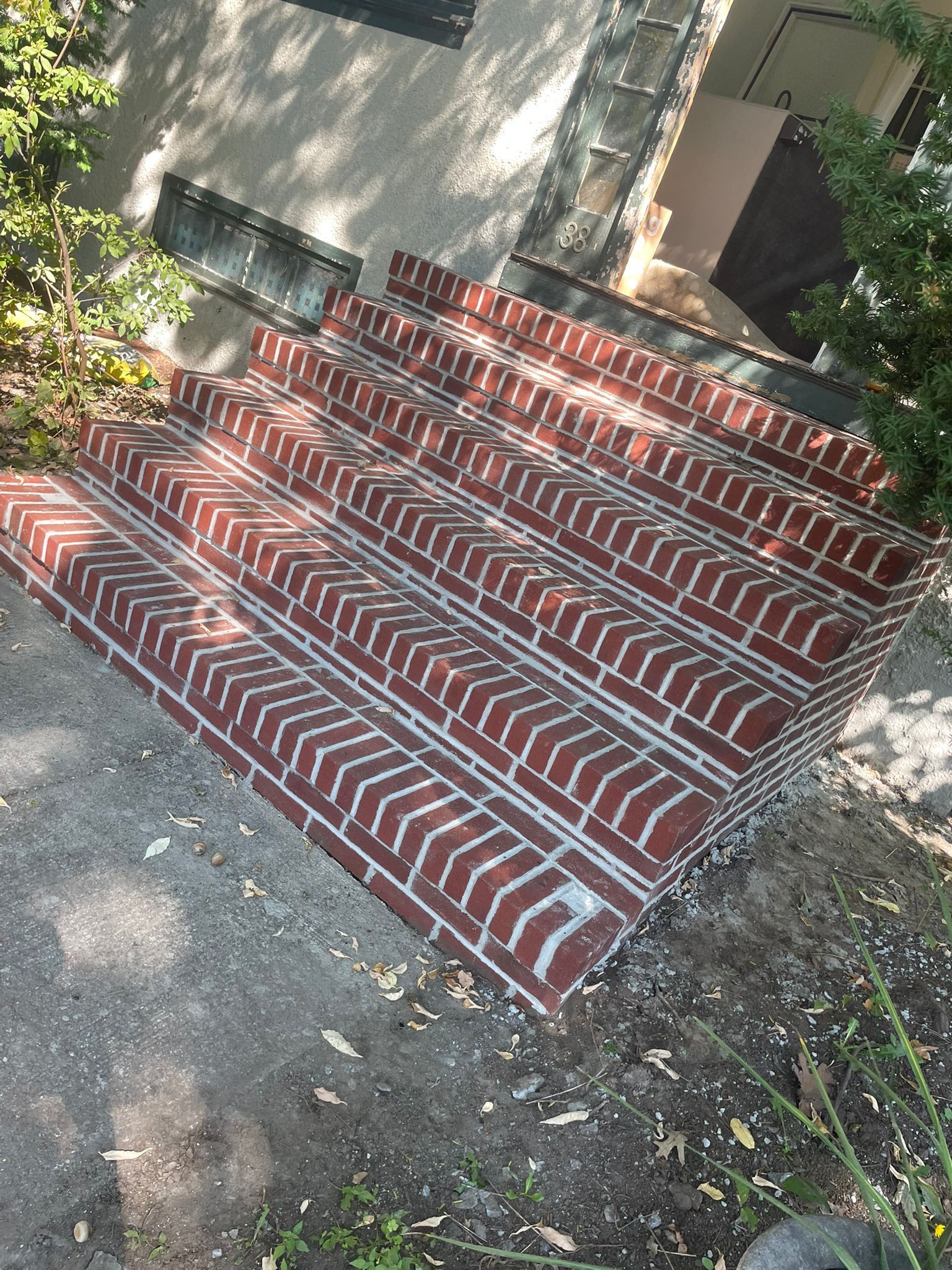 Red brick steps leading to a building, set in concrete, with sunlight casting shadows.