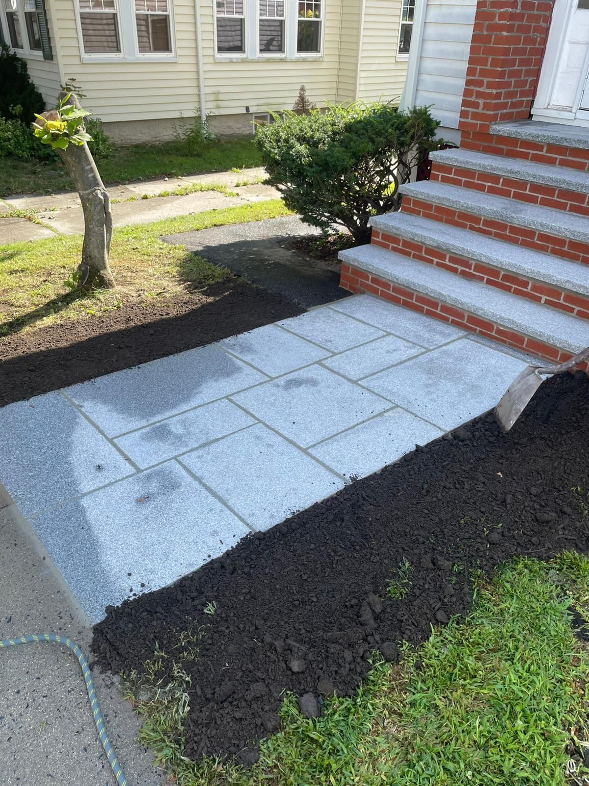 A newly installed walkway made of light grey pavers leads to red brick steps of a house.