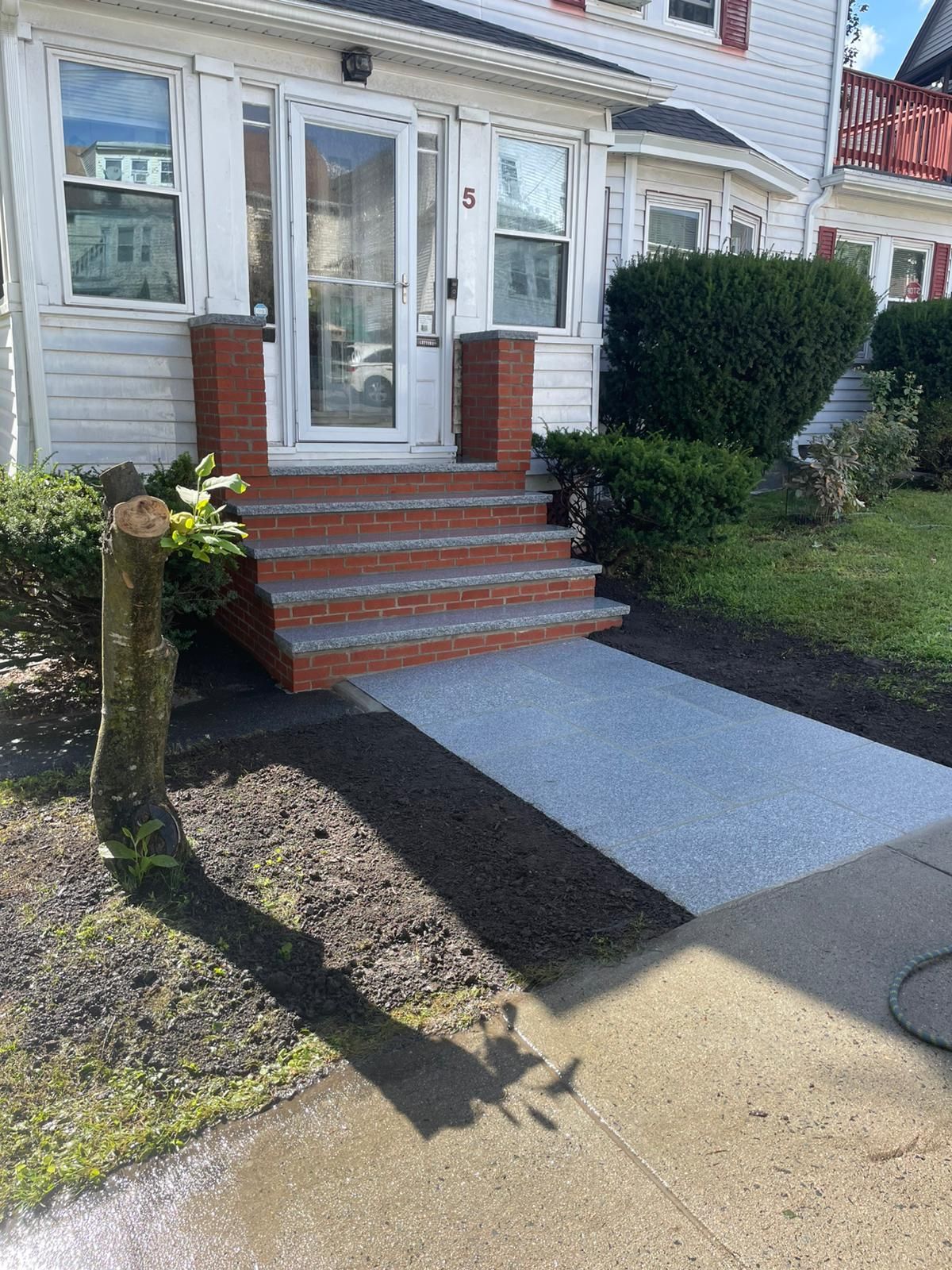 Exterior view of a house with brick steps, a paved walkway, and a trimmed bush.