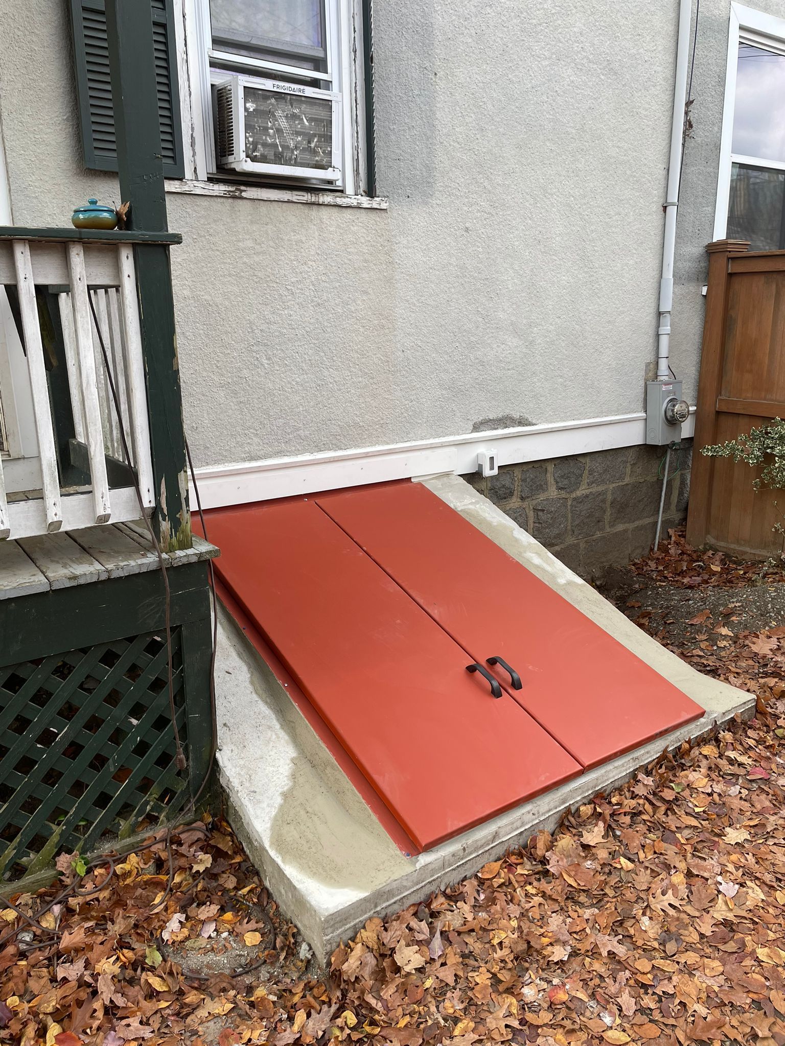 Orange cellar doors built into concrete foundation of a house.