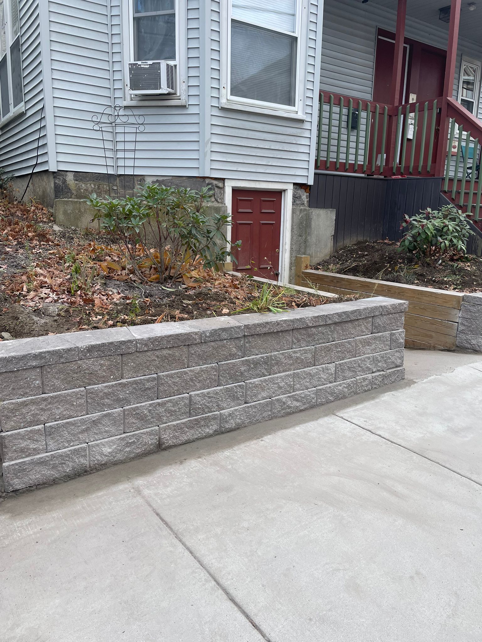 Gray retaining wall in front of a light blue building with a brown door and steps.