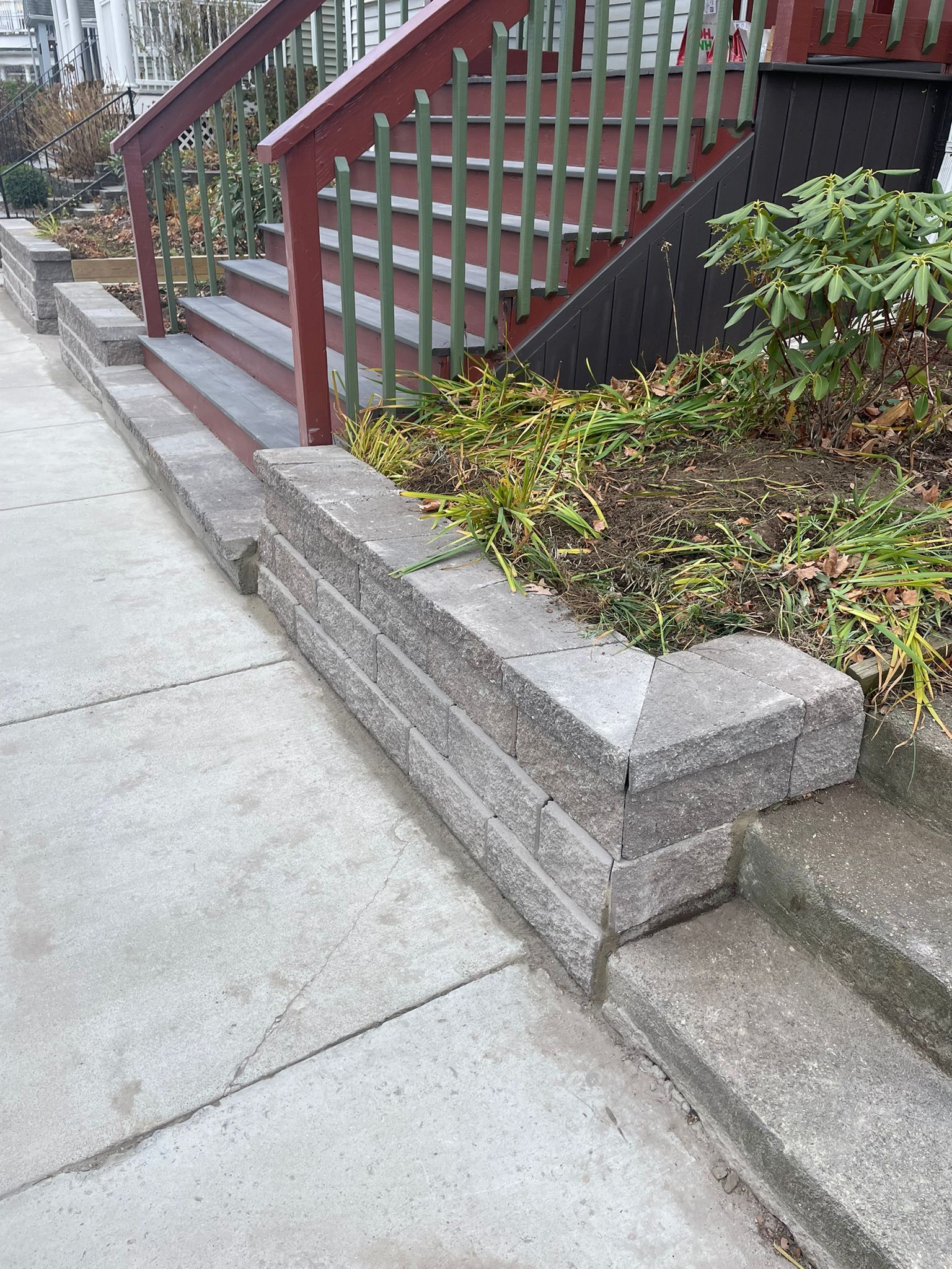 Stone retaining wall and stairs lead up to a house with red railing.