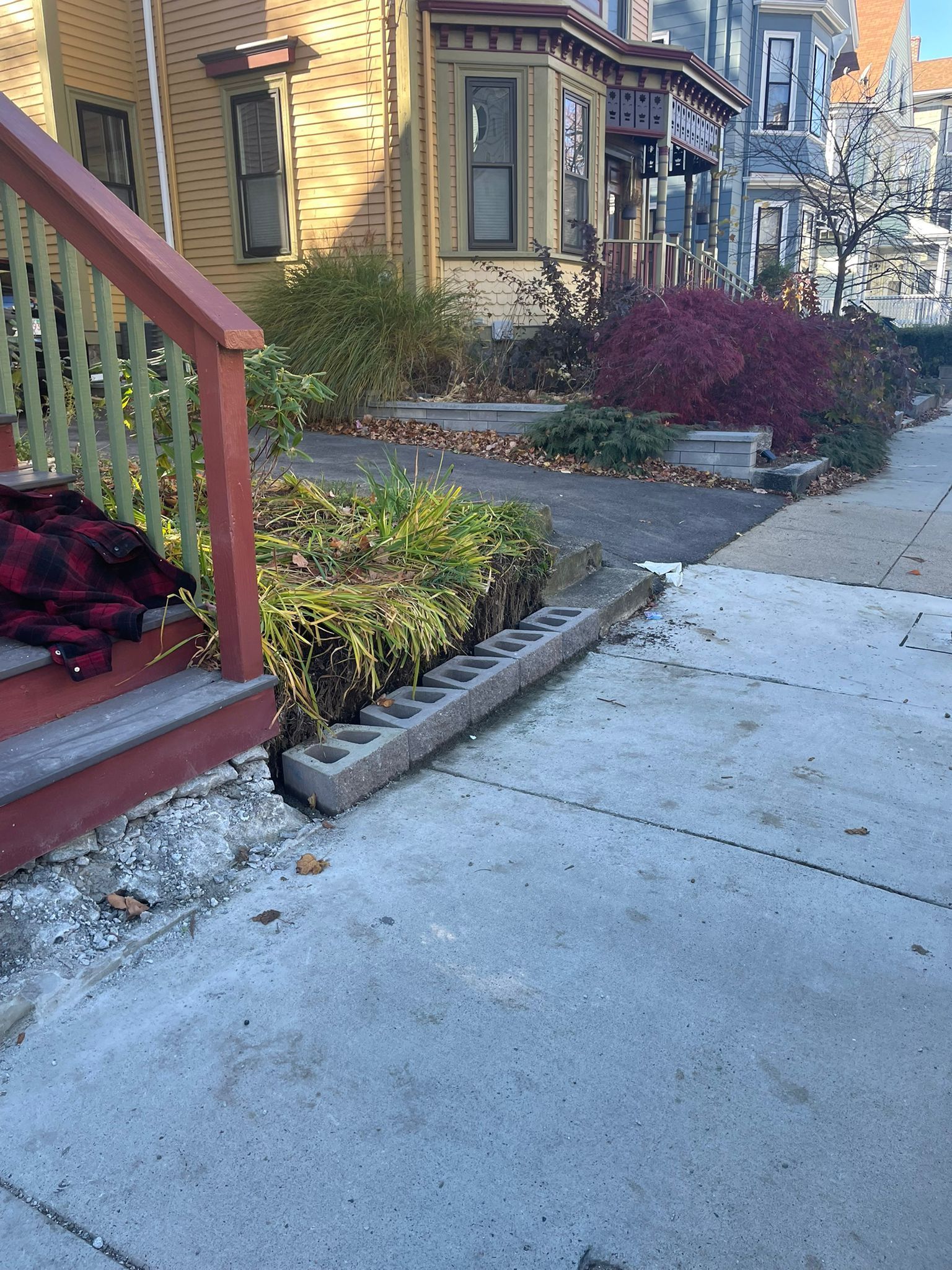 Sidewalk alongside a residential building with a raised garden bed and stairs.