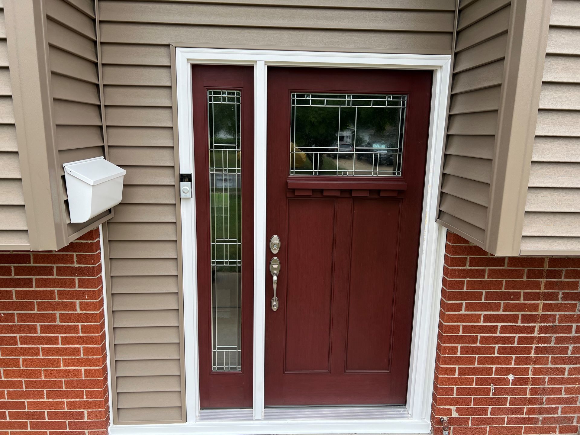 Front entrance of a house with a red door, white siding, brick accents, and tree leaves in the foreground