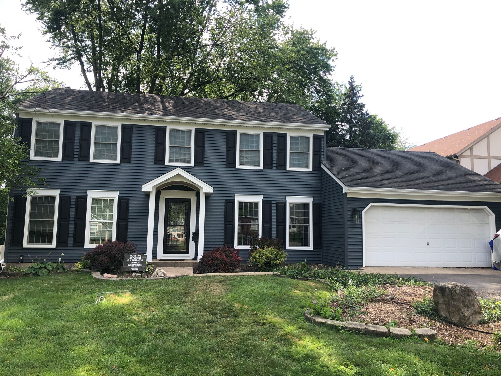 Two-story dark blue house with white trim, a front porch, attached garage, and green lawn