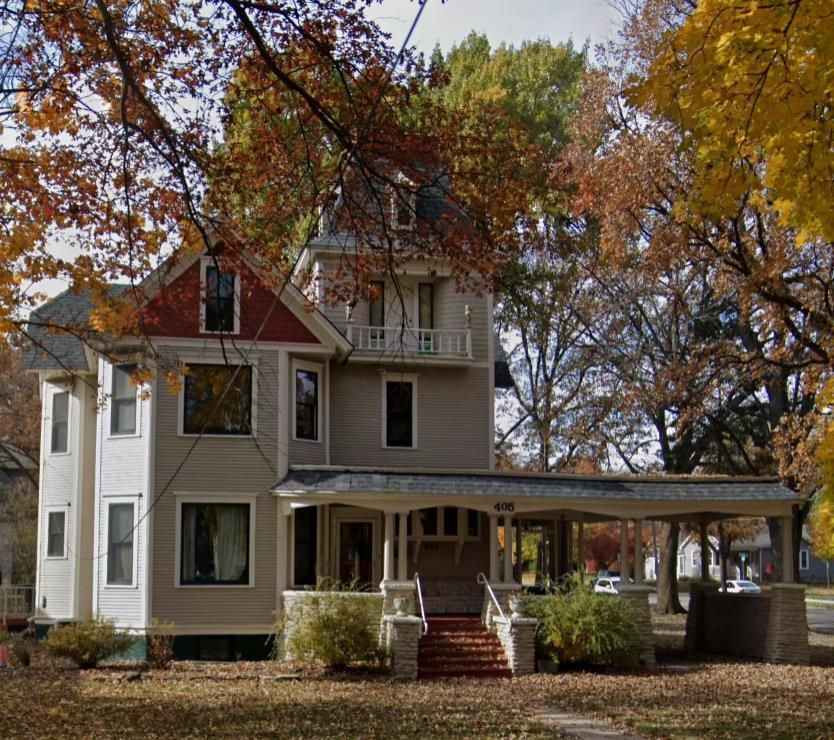 Victorian house with wraparound porch, framed by autumn trees and fallen leaves