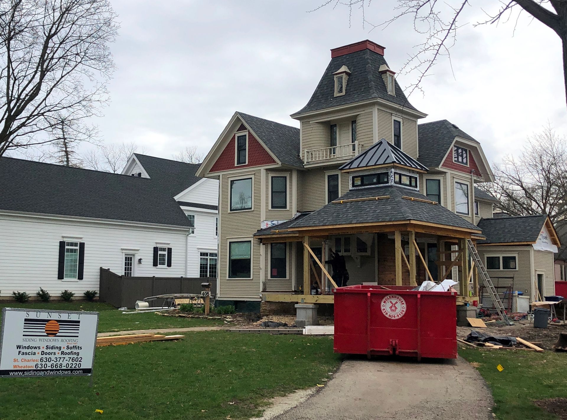 Victorian house under renovation with a red dumpster in front and bare trees around it