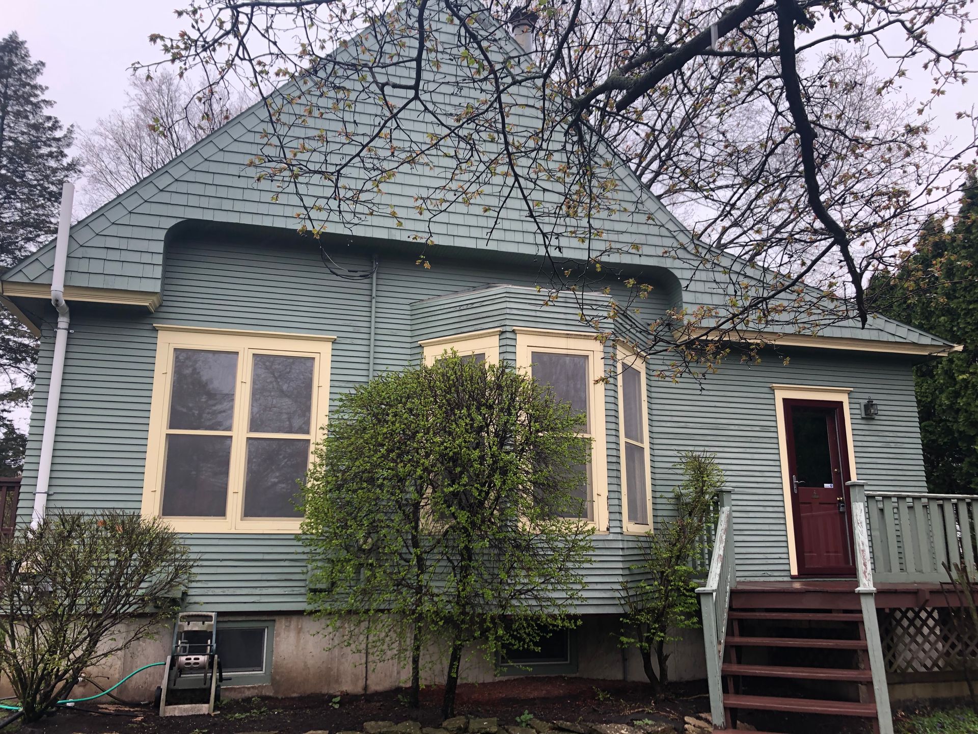 Small green house with a steep roof, beige-trimmed windows, and a red front door amid bare trees.