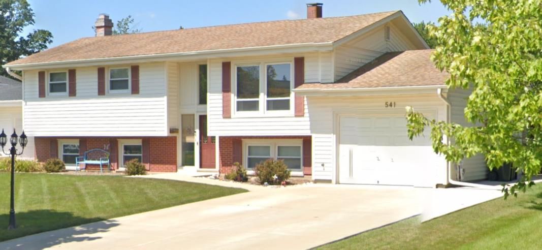Suburban split-level house with white garage, brick facade, and a sloped driveway under a clear sky