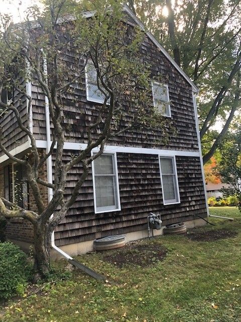 Two-story shingled house with white-trim windows and a tree in the front yard