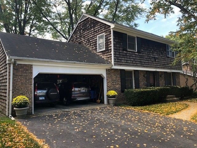 Suburban house with open two-car garage, black SUV, brick and shingle exterior, and autumn leaves on driveway