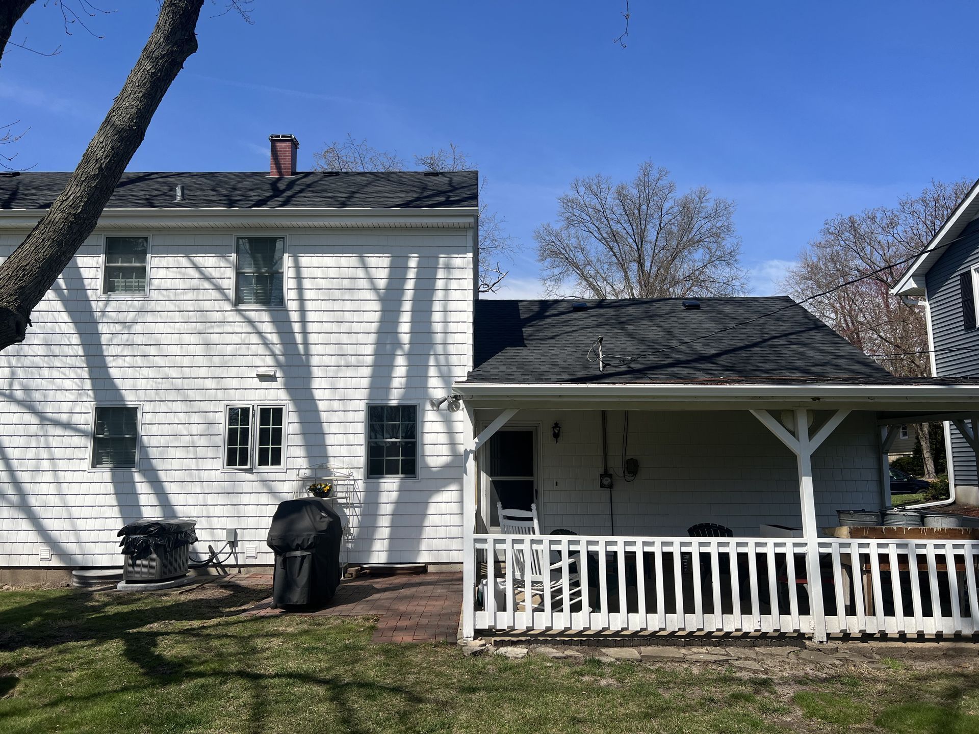 White house with dark roof and front porch, seen from the yard on a sunny day