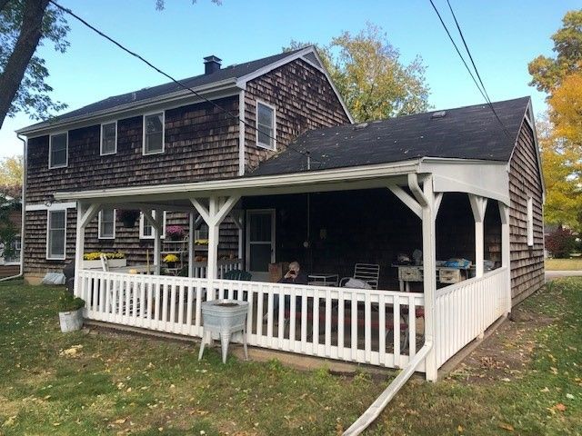 Two-story house with white porch railing and covered deck, viewed from the yard in autumn