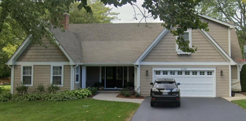Suburban house with gray siding, two-car garage, and a black car parked in the driveway