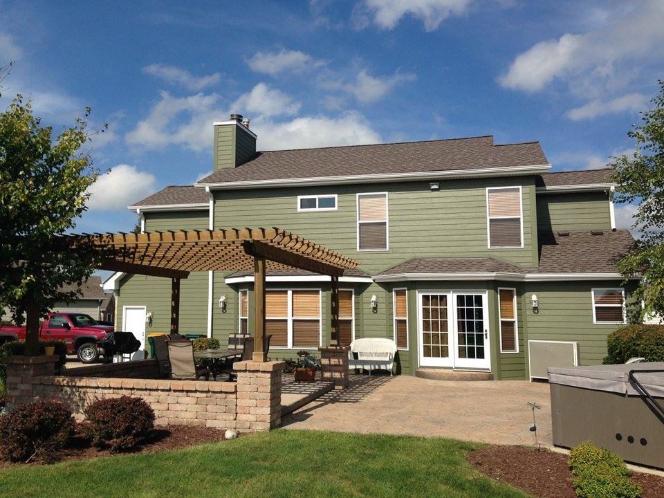 Backyard patio with pergola, brick seating wall, and two-story house under a blue sky