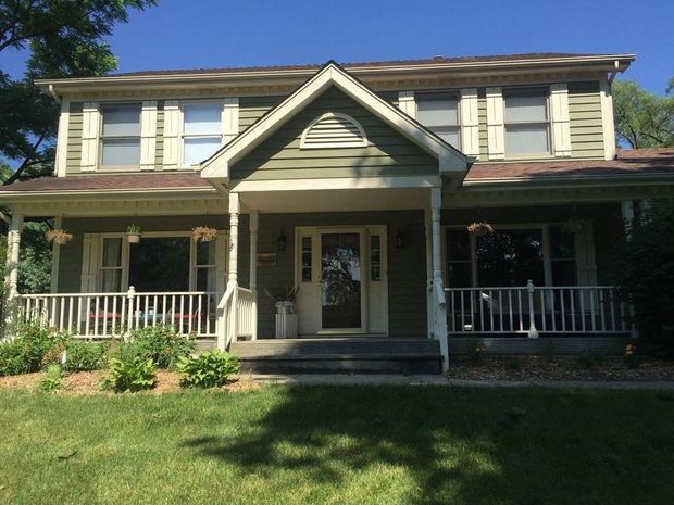 Two-story beige house with a front porch, white trim, and green lawn in daylight