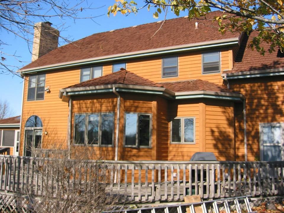 Two-story orange wooden house with a screened porch and leafless trees in front