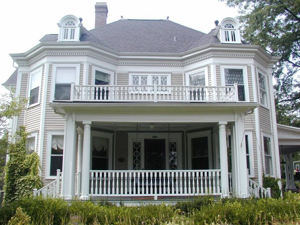 Front view of a two-story white house with a large porch and balcony, framed by trees.