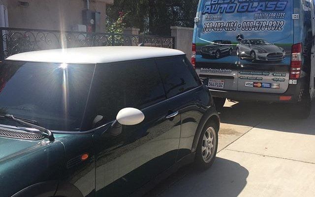 A green car is parked next to a van that says auto glass