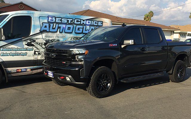A black truck is parked next to a best choice auto glass van.