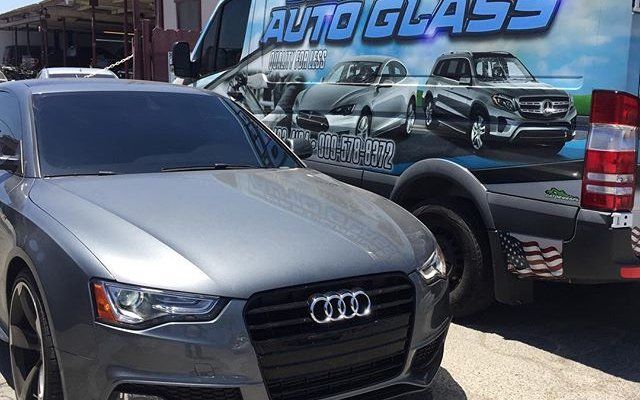 A gray audi is parked in front of an auto glass truck.