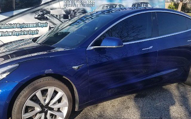 A blue tesla model 3 is parked on the side of the road.