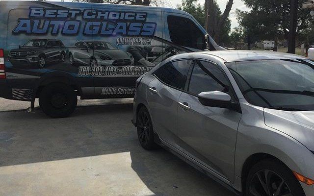 A silver car is parked next to a best choice auto glass van