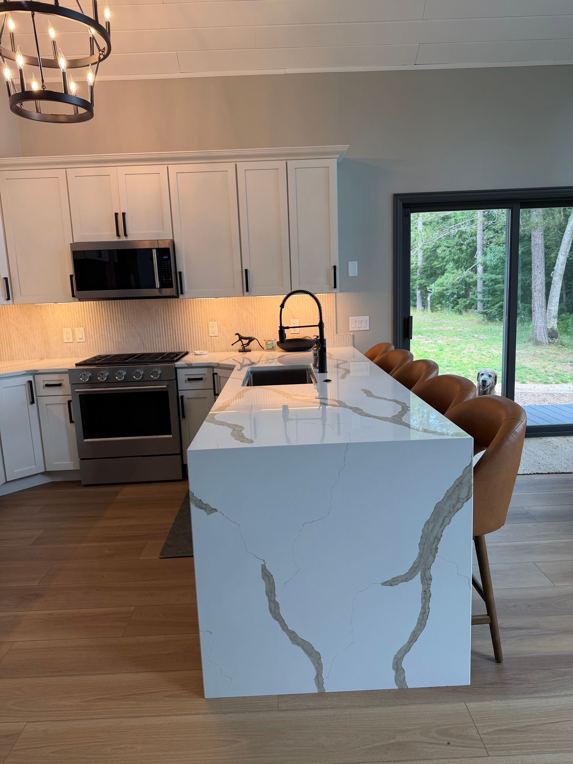 Modern kitchen with white cabinets, marble island, wood floor, and sliding glass doors to greenery