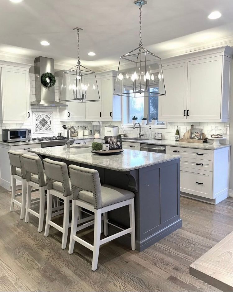A kitchen with white cabinets, a large island, and stools.